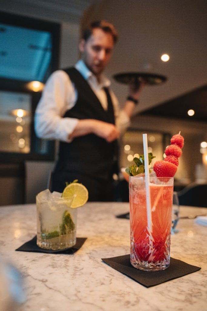 Vibrant cocktails on a marble counter with a blurred waiter in a Scottish bar setting.